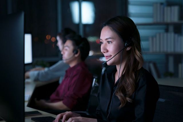 A woman wearing a headset is sitting in front of a computer.