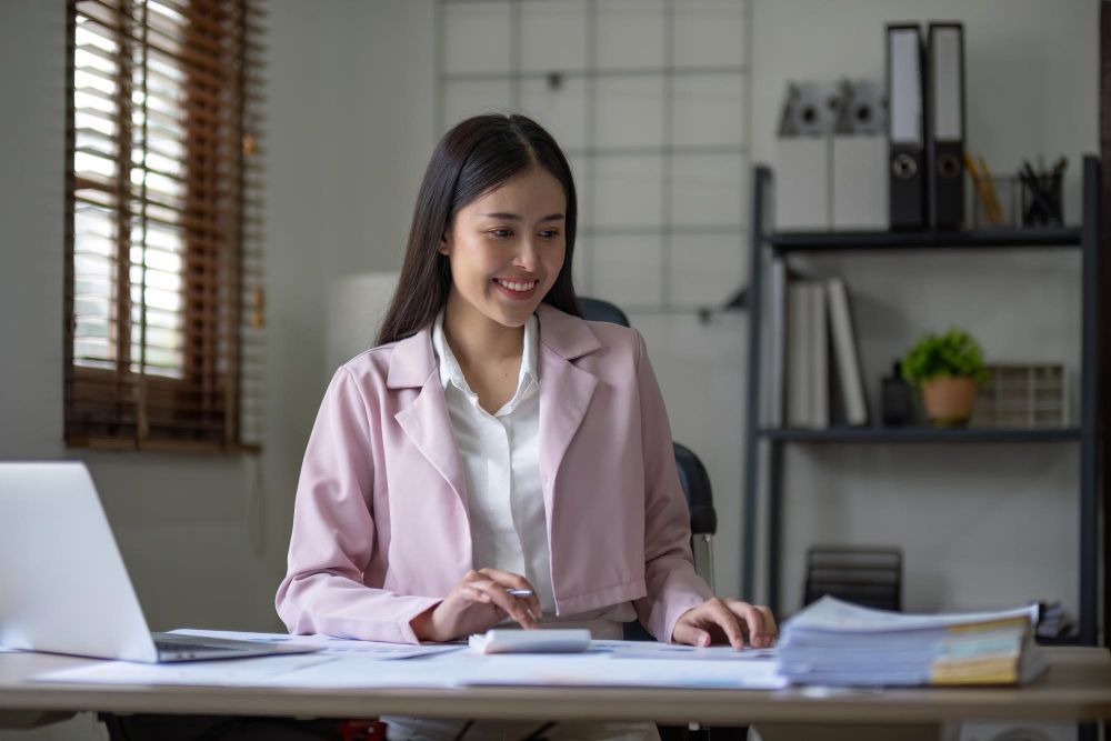 A woman is sitting at a desk with a laptop and a calculator.