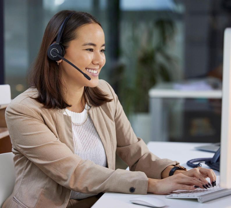 A woman wearing a headset is sitting in front of a computer.