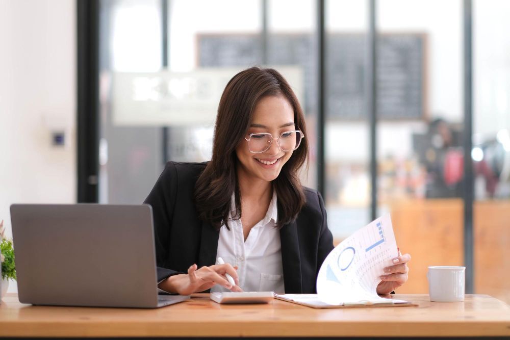A woman is sitting at a desk with a laptop and a calculator.