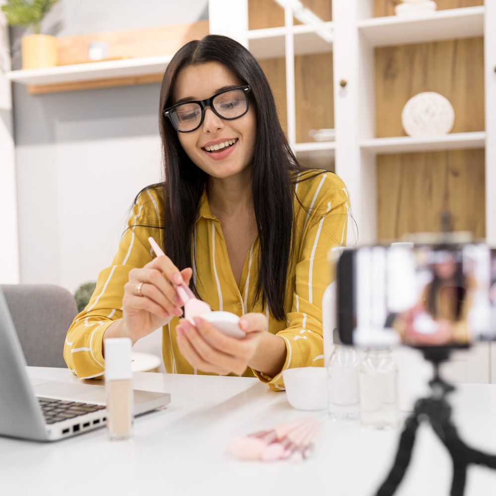 A woman is sitting at a table with a laptop and a cell phone.
