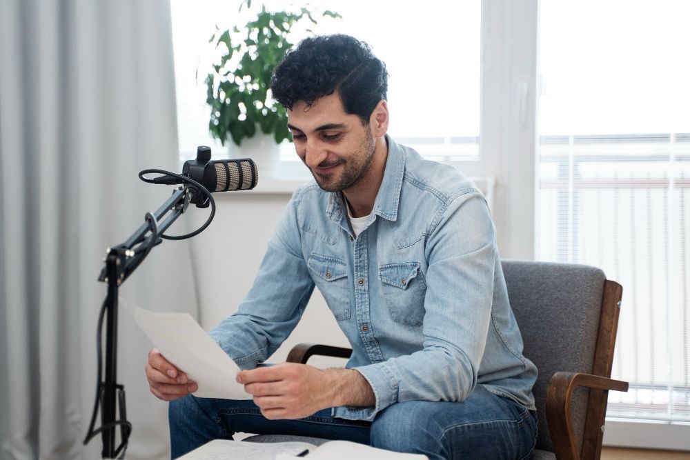 A man is sitting in a chair holding a piece of paper in front of a microphone.