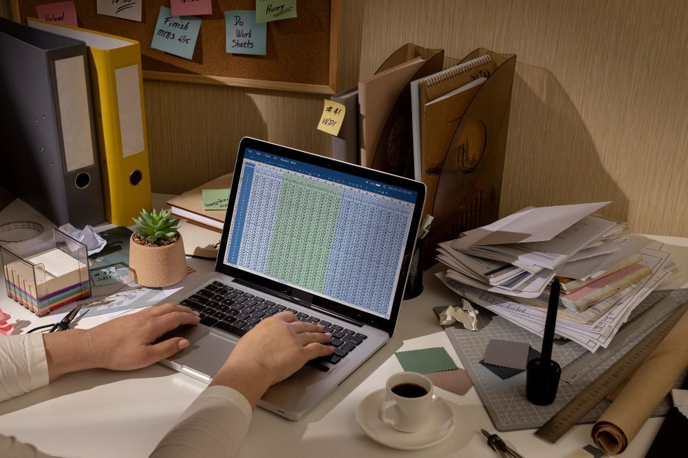A person is typing on a laptop computer at a messy desk.