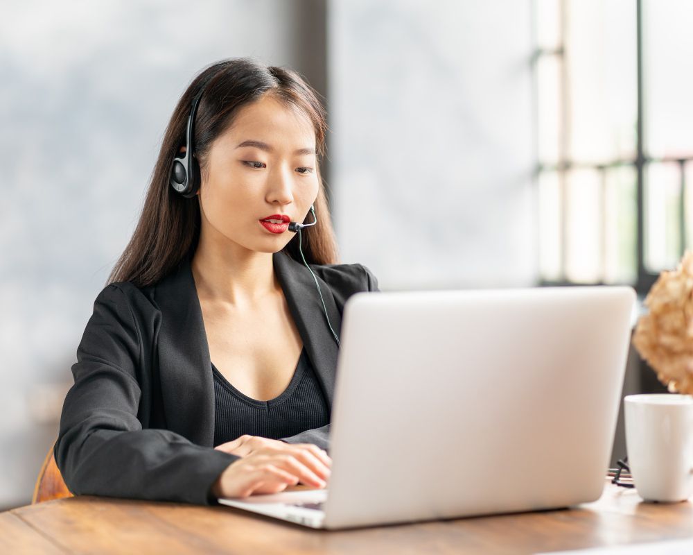 A woman wearing a headset is sitting in front of a laptop computer.