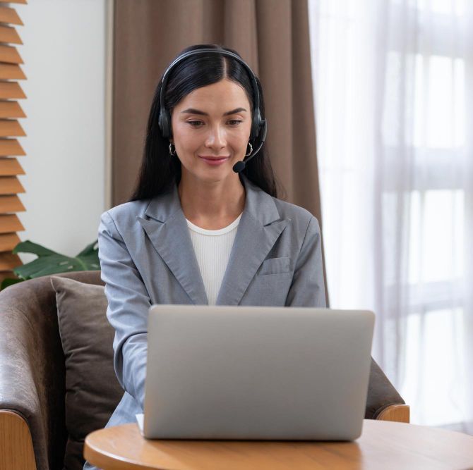A woman wearing headphones is sitting at a table using a laptop computer.