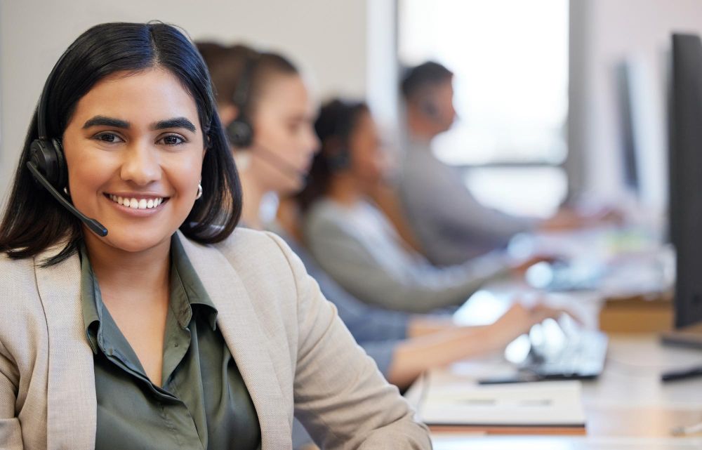 A woman wearing a headset is sitting at a desk in a call center.
