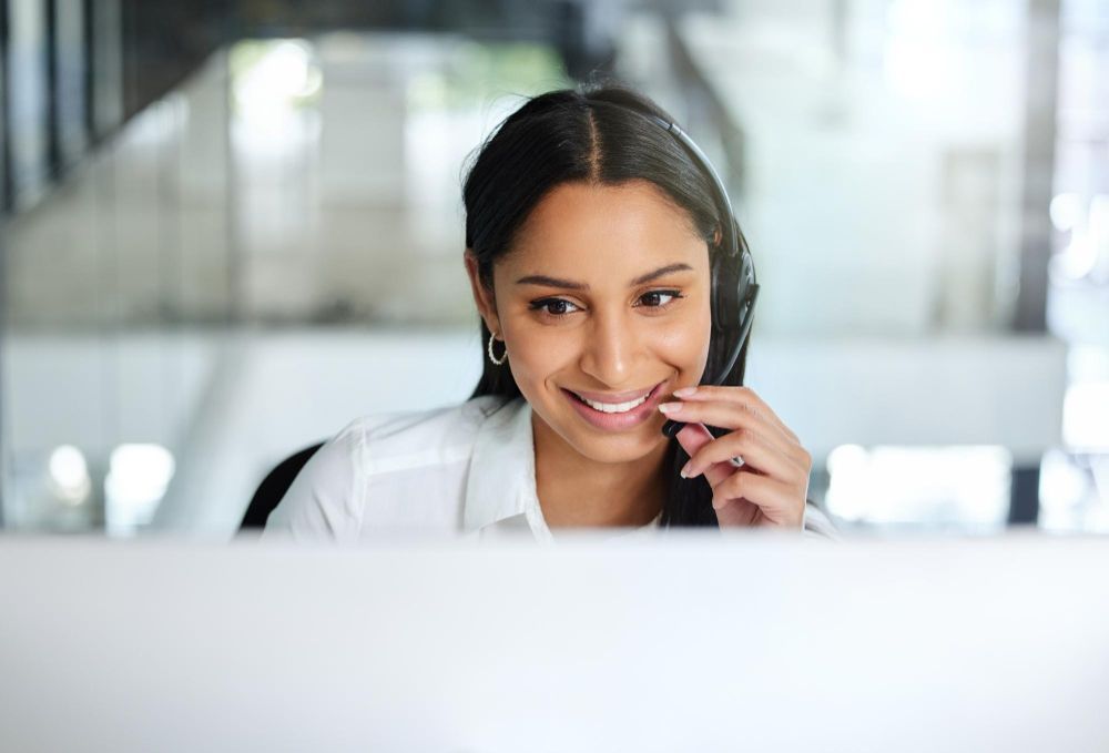 A woman is talking on a headset while sitting in front of a computer.