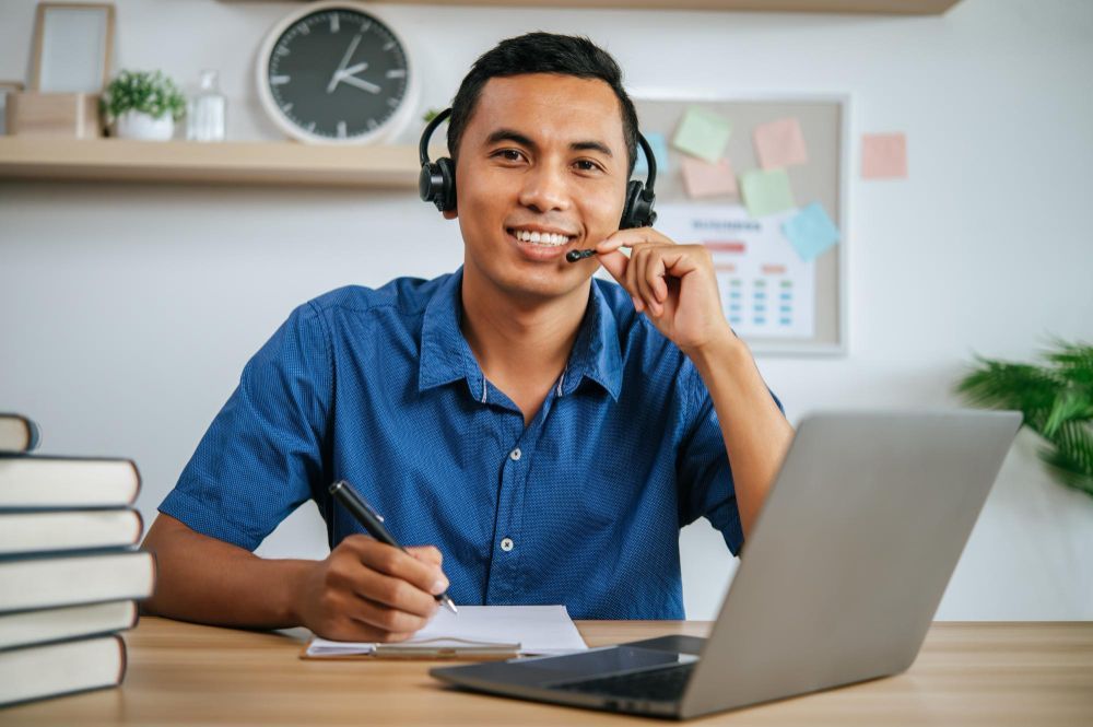 A man wearing headphones is sitting at a desk with a laptop.