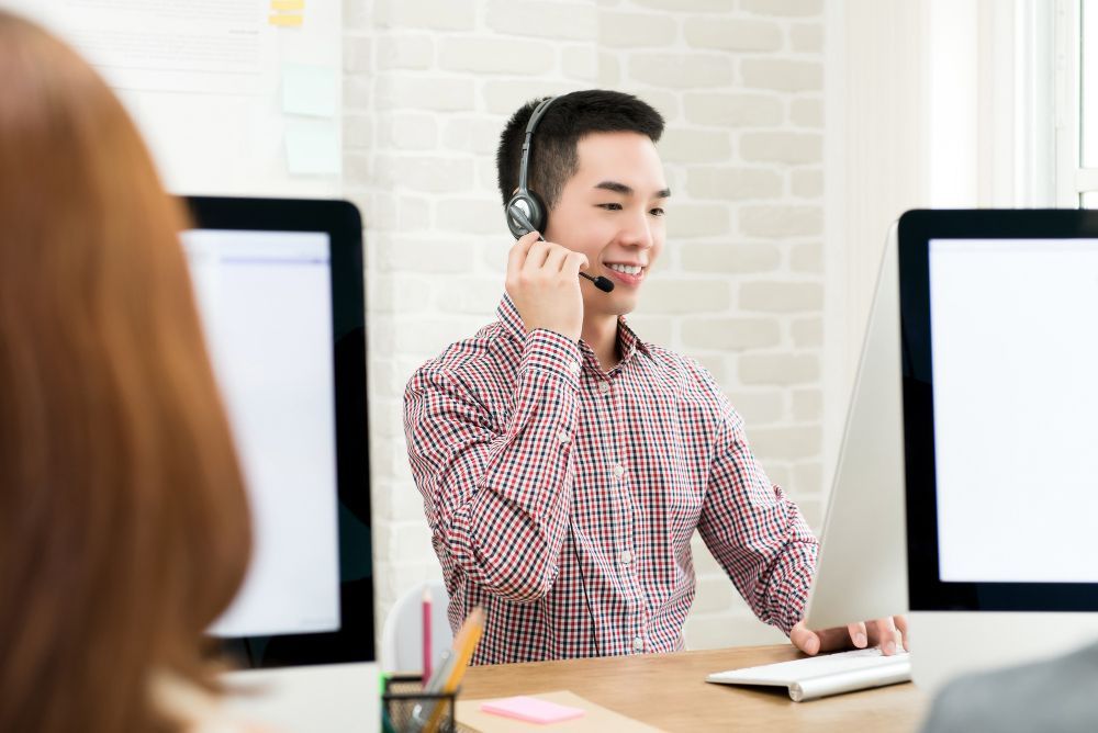 A man wearing a headset is sitting at a desk in front of a computer.