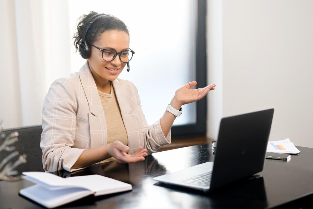 A woman wearing headphones is sitting at a desk in front of a laptop computer.