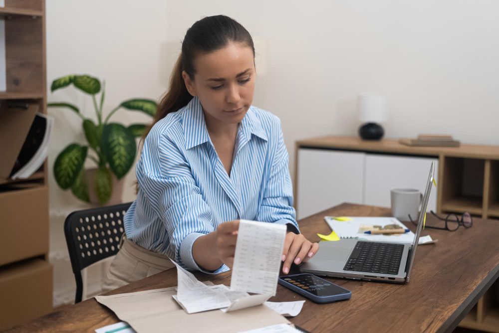 A woman is sitting at a desk with a laptop and a receipt.
