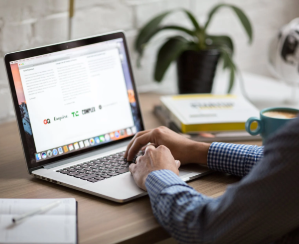 A man is typing on a laptop with a cup of coffee in the background