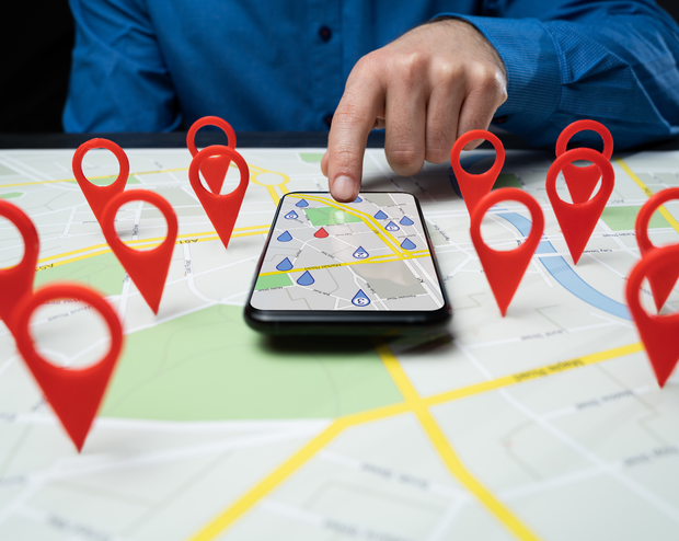 A person is pointing at a cell phone on a map surrounded by red pins.