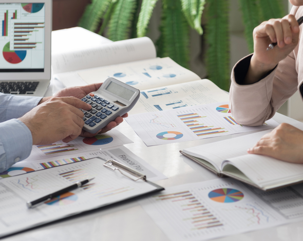 A man is using a calculator while a woman looks at a laptop.