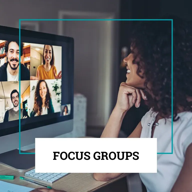 A person smiling while looking at a monitor displaying a video conference of four people, labeled 