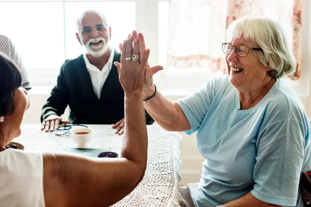 Three people are smiling while giving each other a high-five across a table in a bright room.