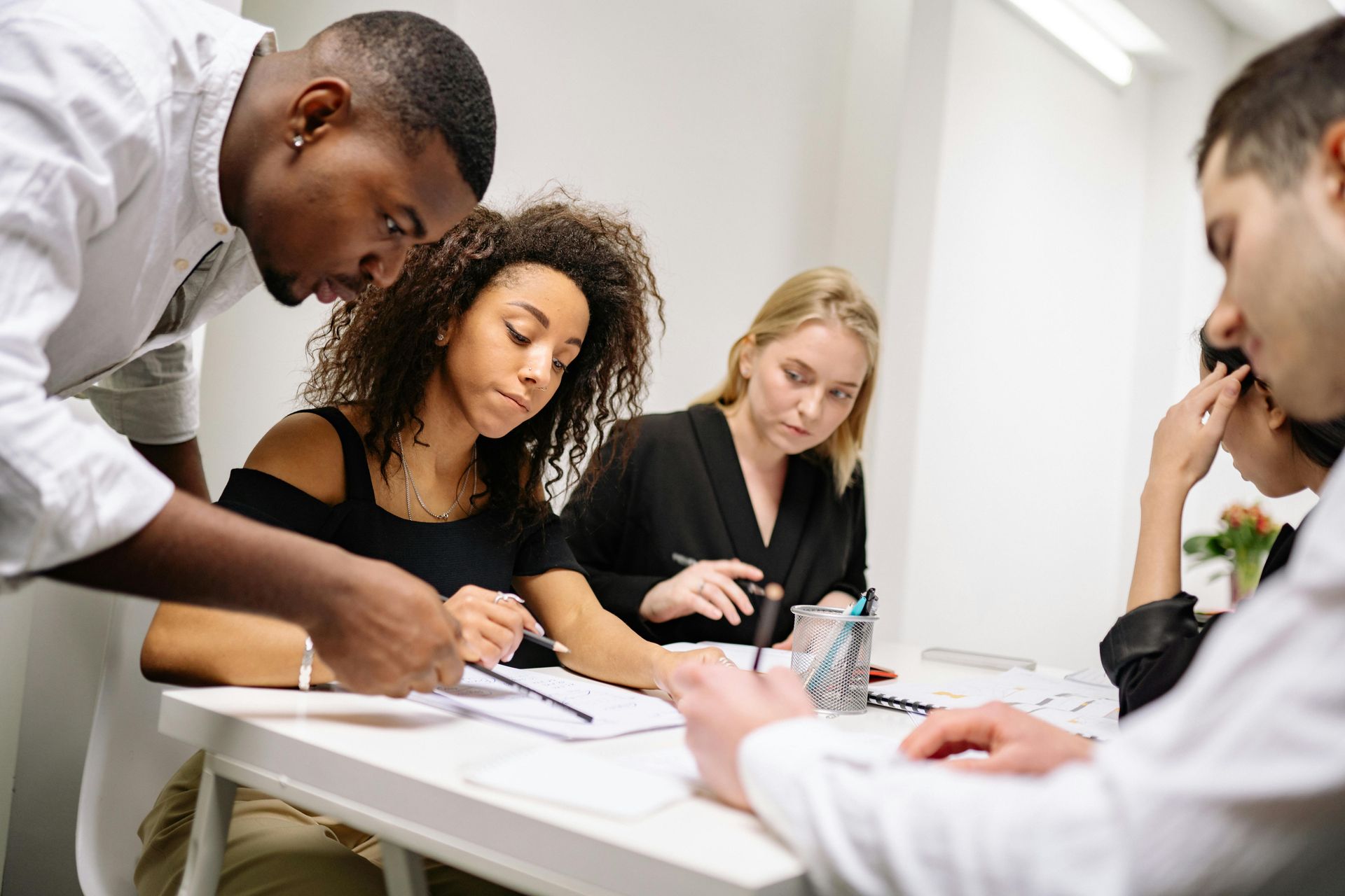 Four people collaborate around a white desk, examining papers and working together in a bright, modern office setting.