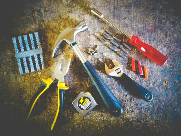 A hammer , pliers , screwdriver , wrench , tape measure and nails are on a table.