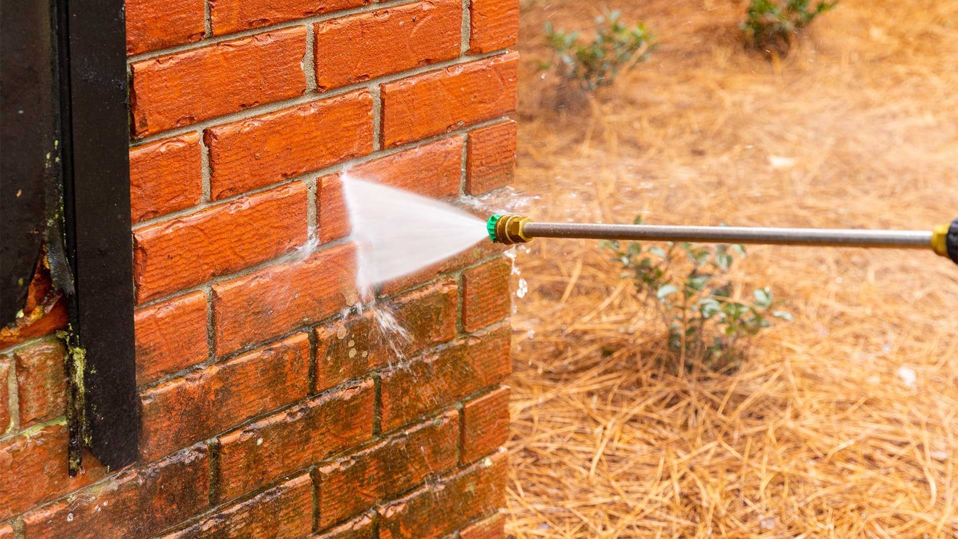 A person is using a high pressure washer to clean a brick wall.