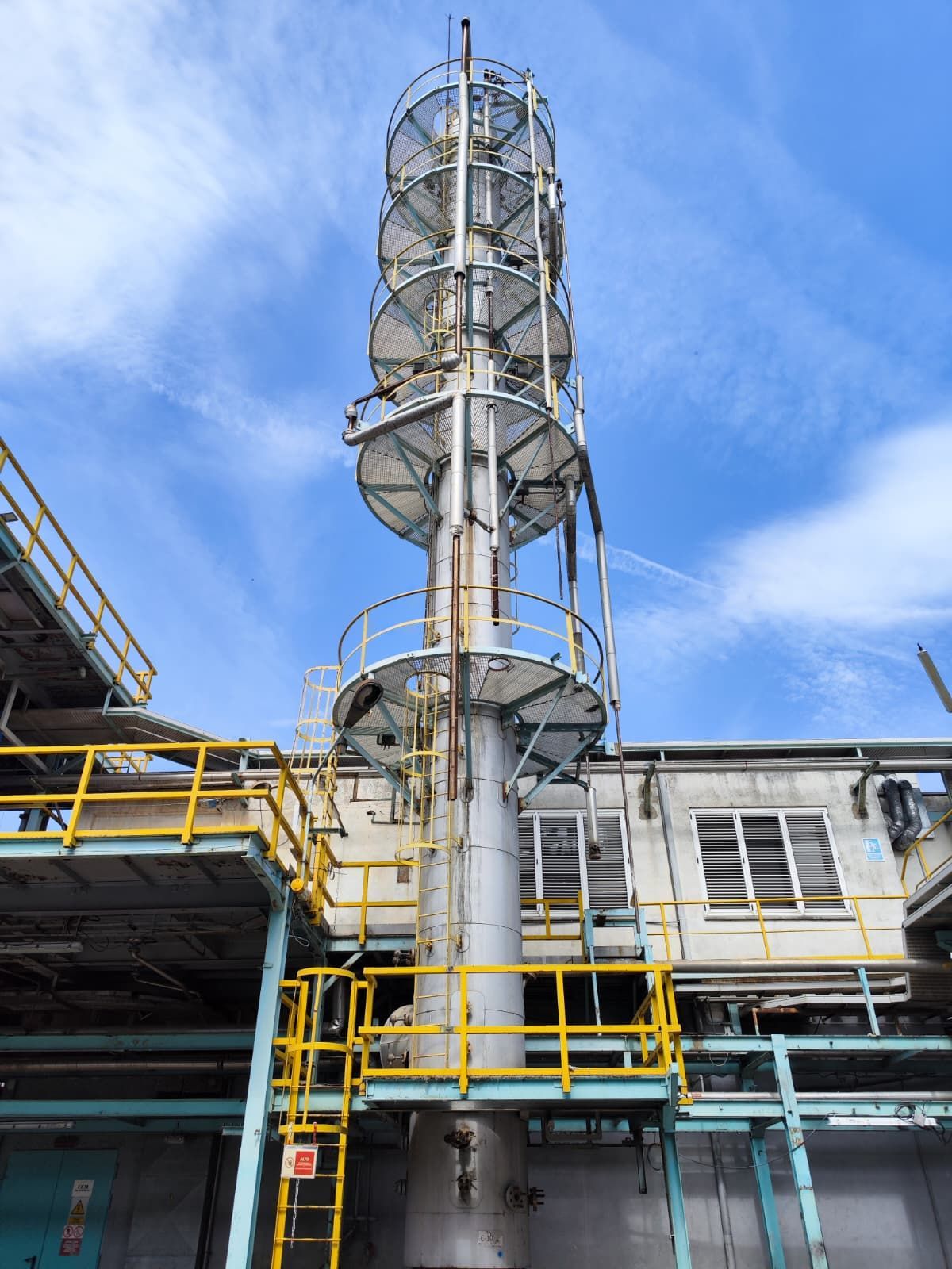 Torre industrial con escalera de caracol exterior contra un cielo parcialmente nublado.