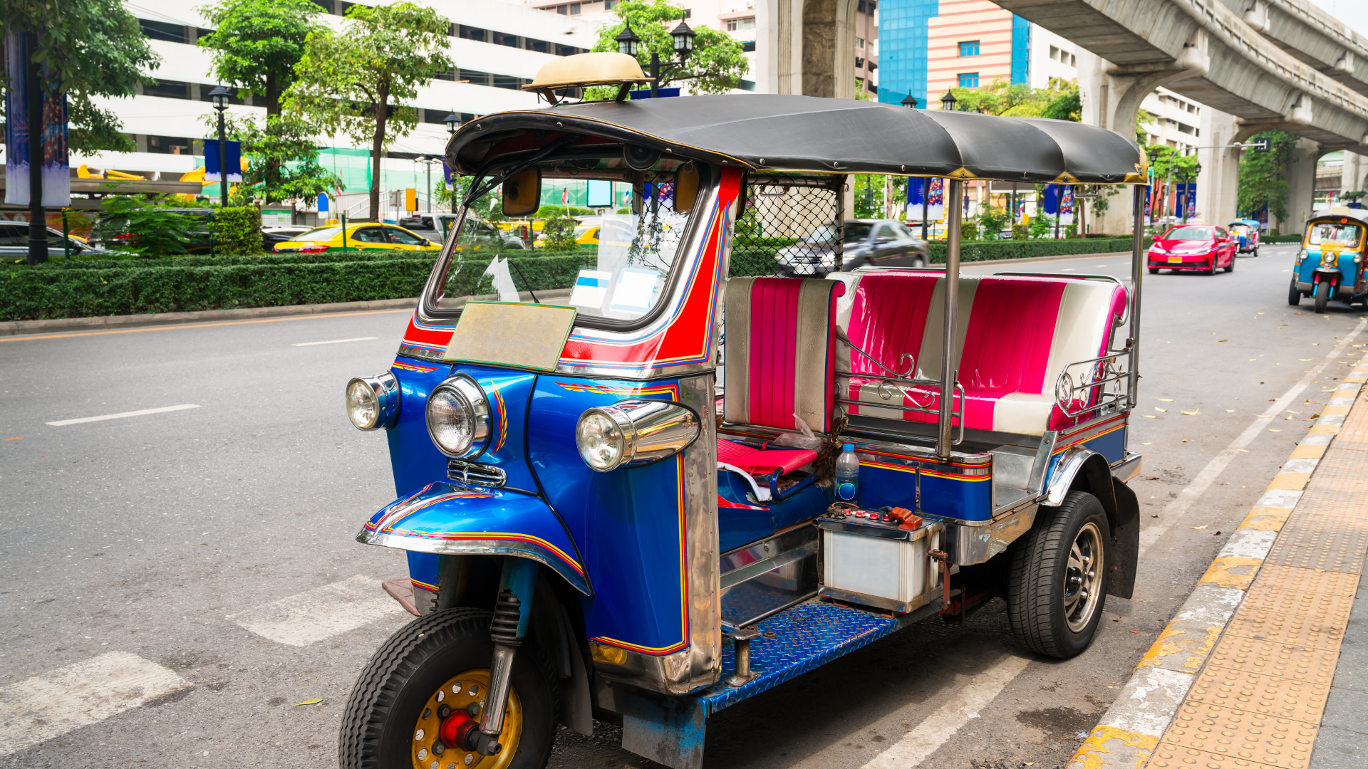 A blue and red rickshaw is parked on the side of the road.