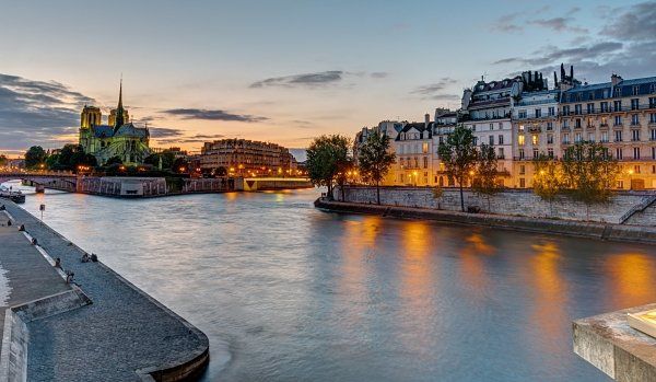 The notre dame cathedral is visible across the river in paris at sunset.