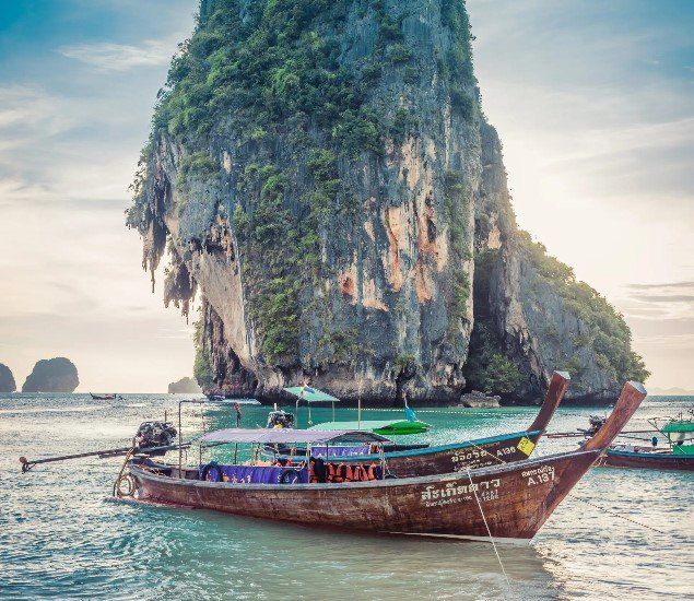 A boat is floating on top of a body of water in front of a large rock.