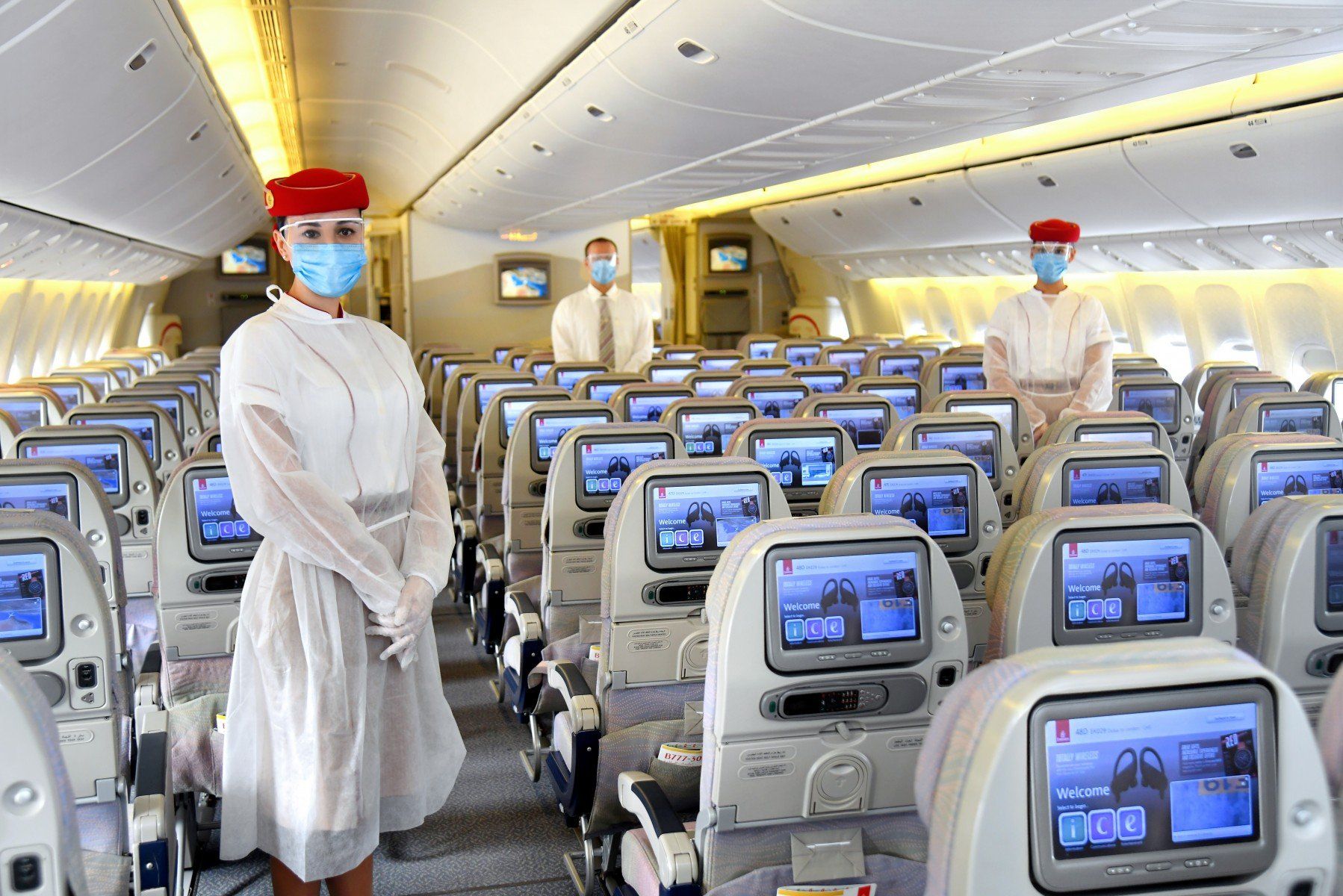 A woman wearing a mask is standing in the middle of an airplane.