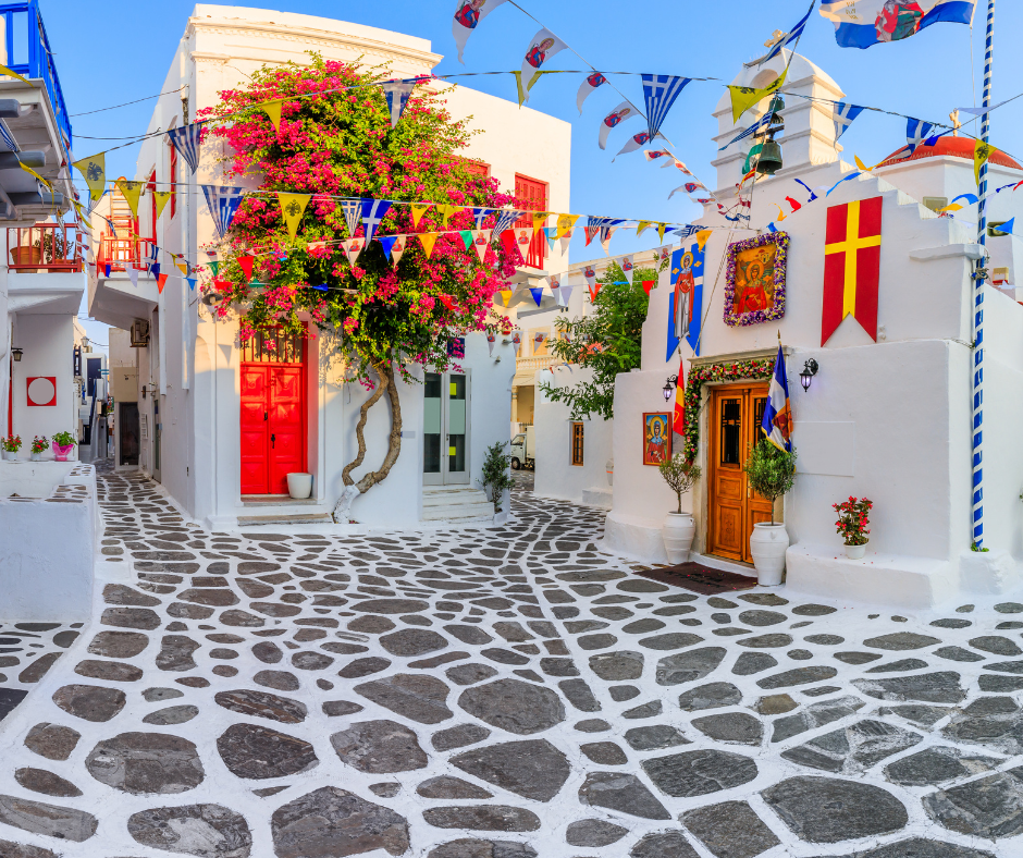 A narrow cobblestone street with white buildings and colorful flags