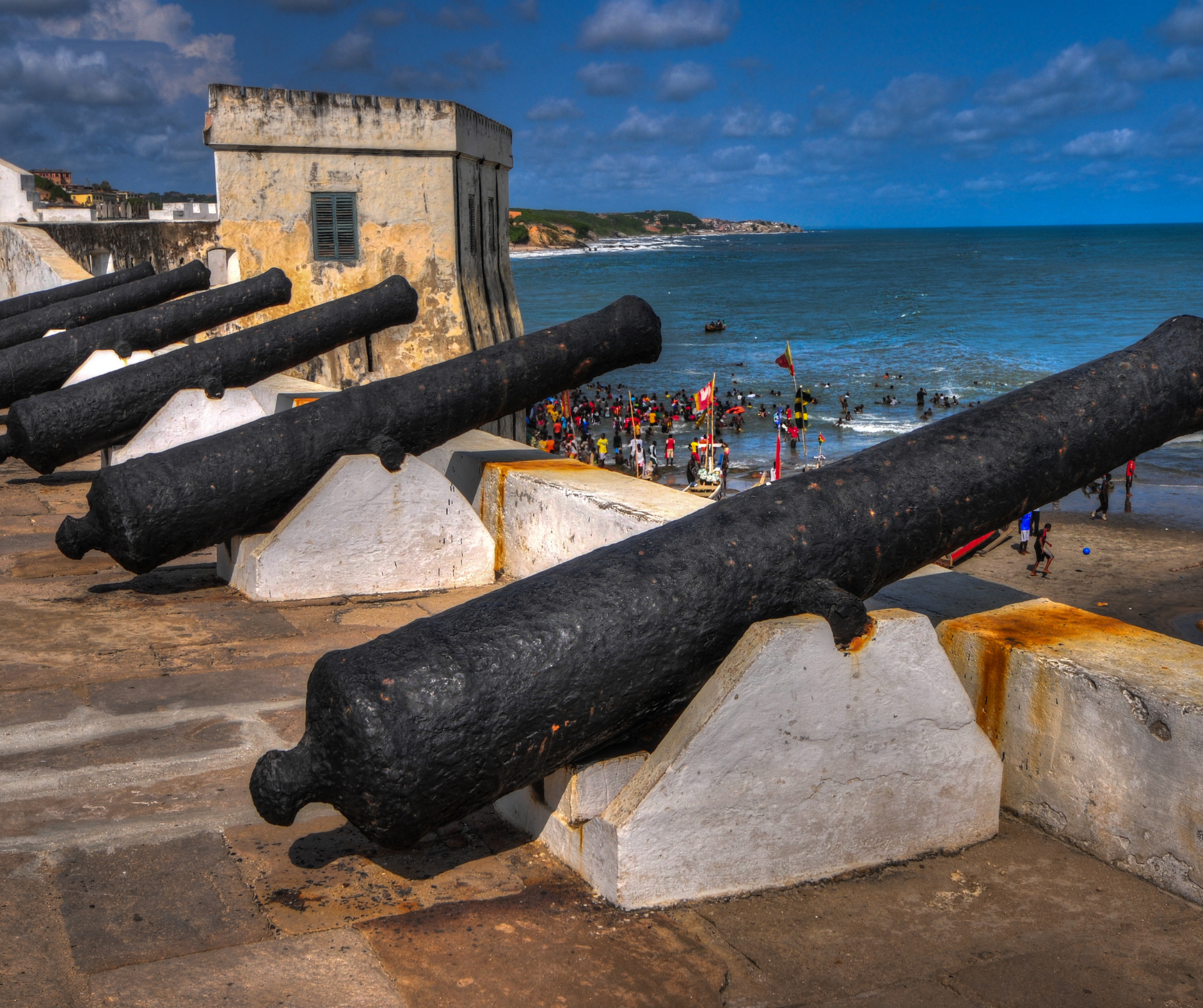 A row of black cannons are sitting on concrete blocks near the ocean