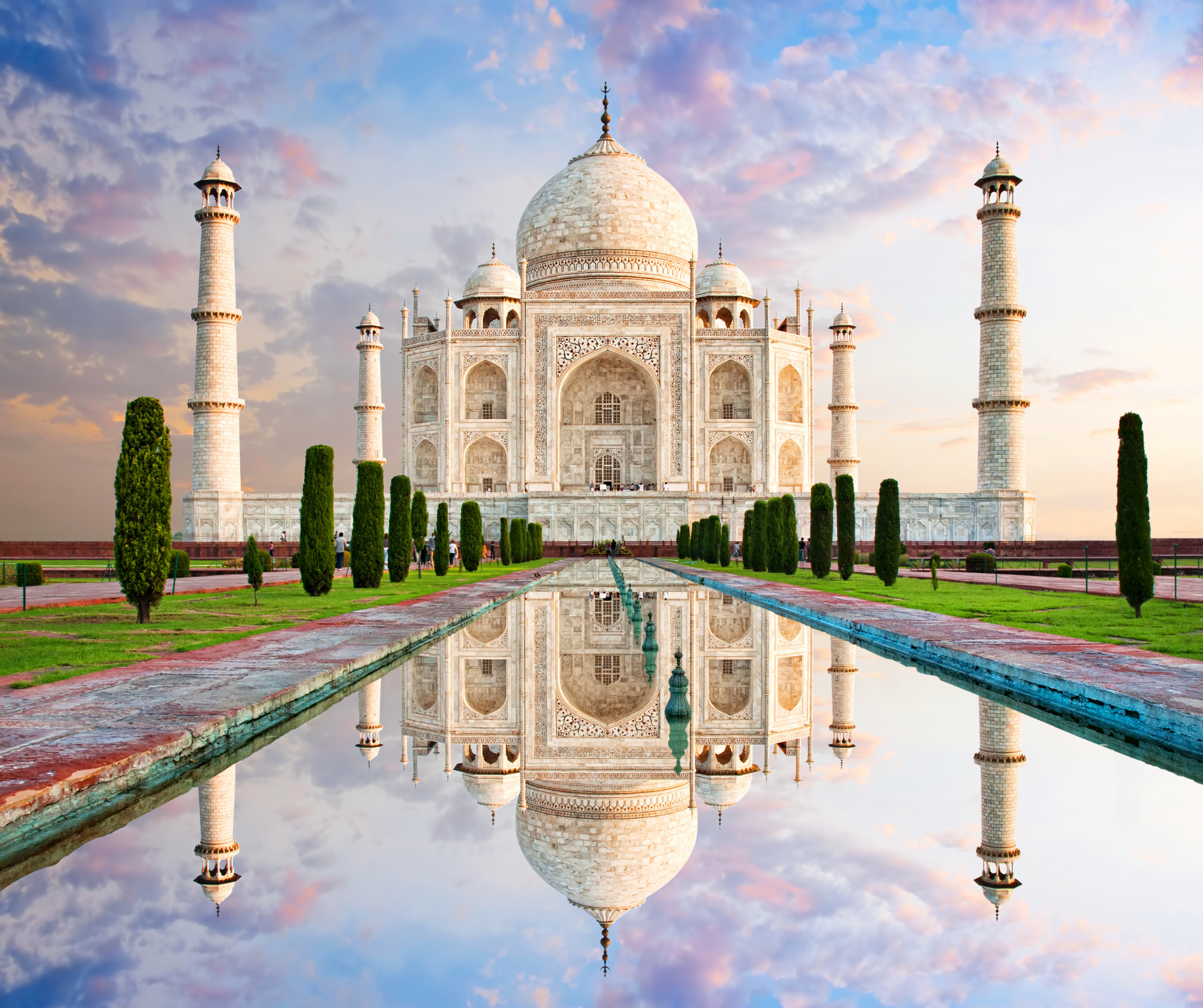 The taj mahal is a very large white building with a pond in front of it.