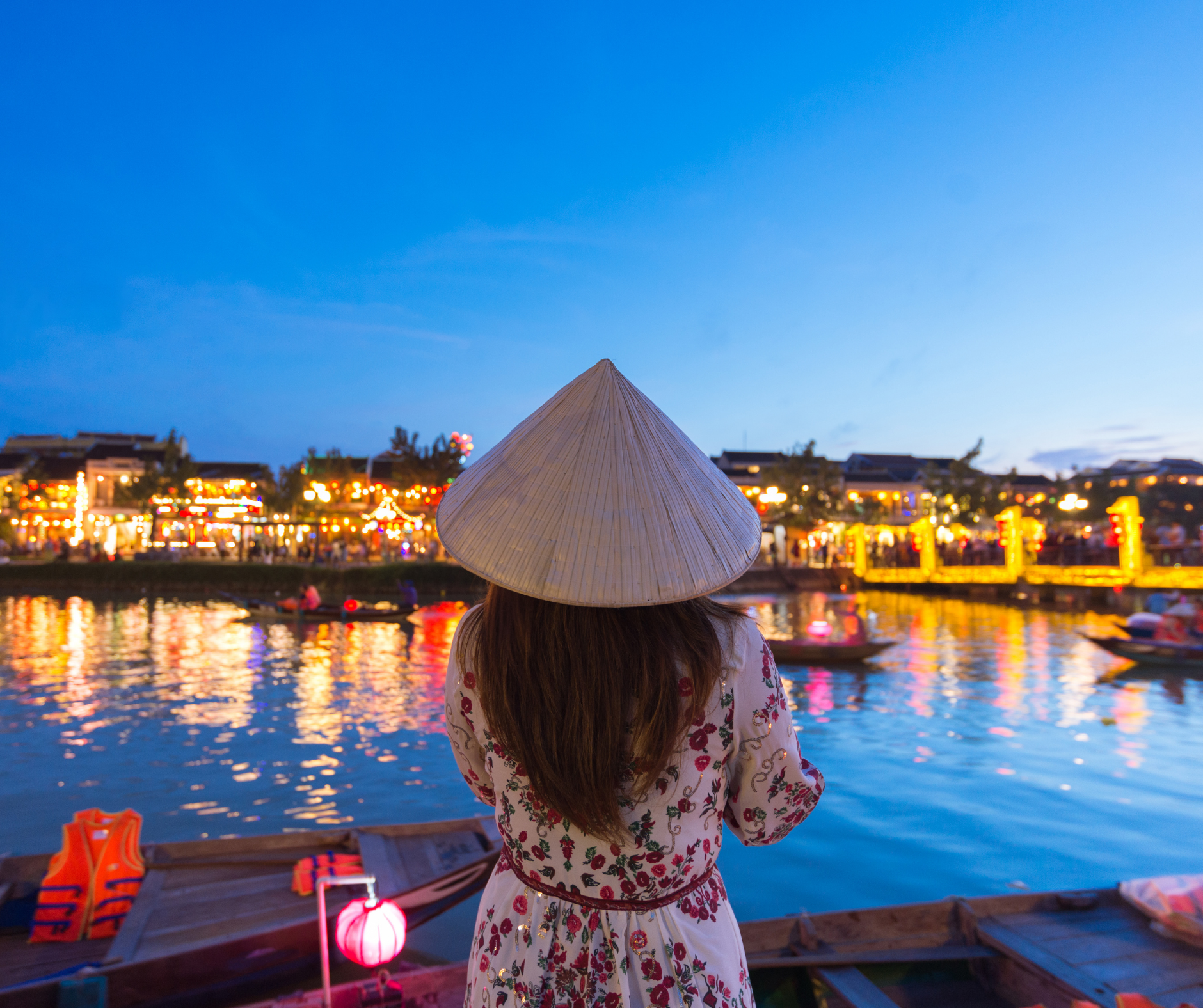 A woman wearing a conical hat is standing next to a body of water.