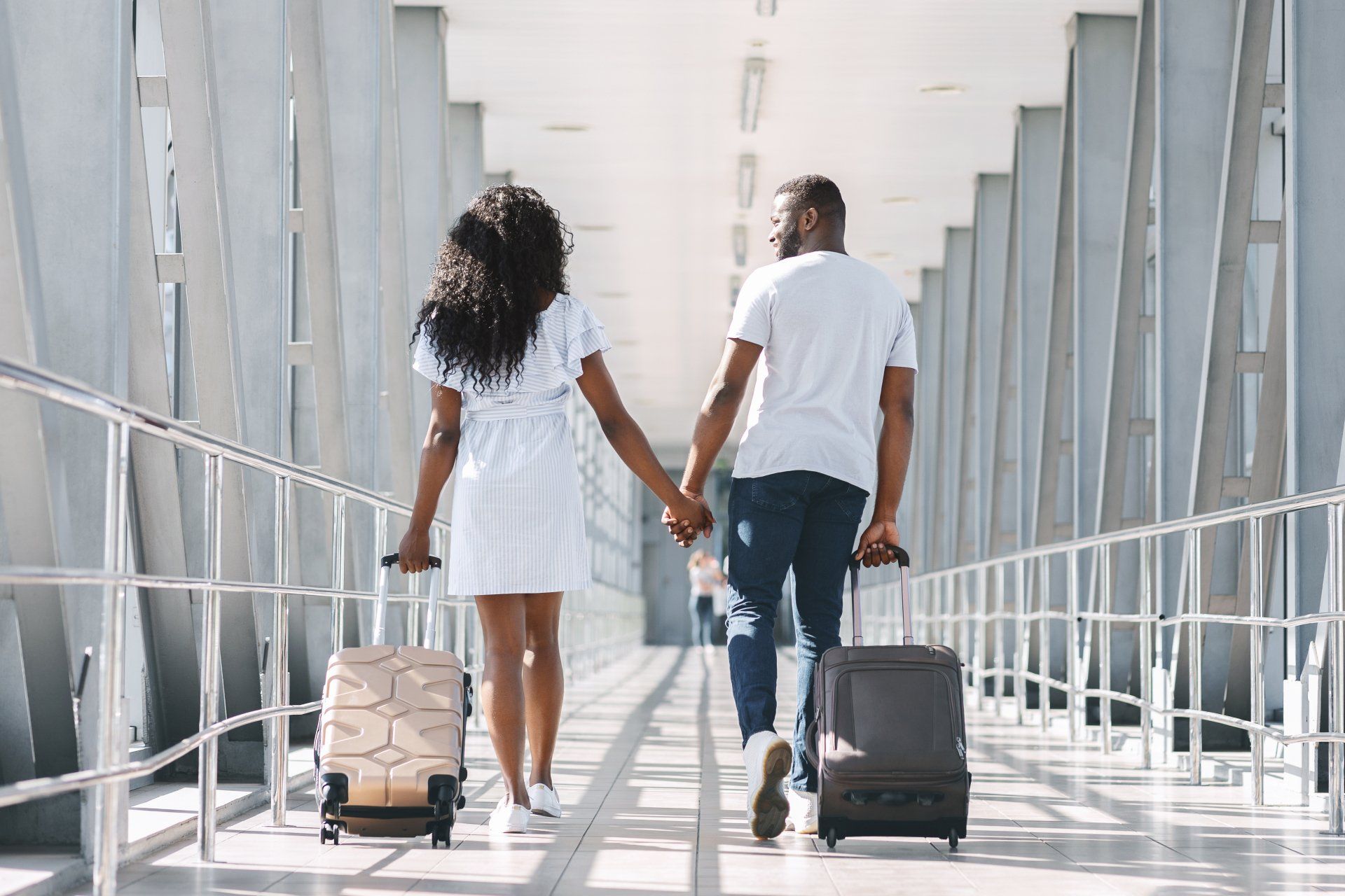 A man and a woman are walking down a bridge with their luggage.