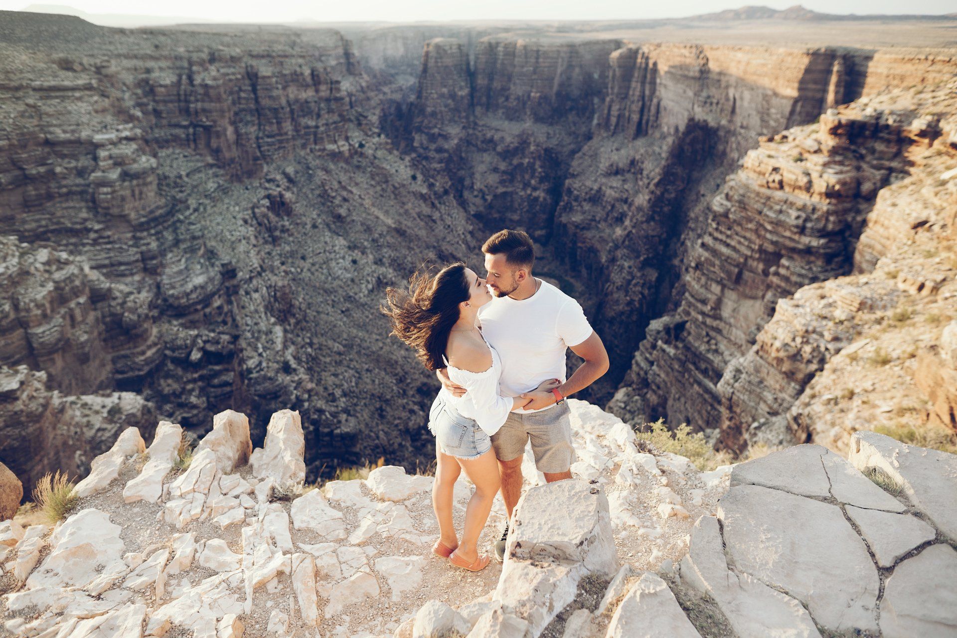 A man and a woman are kissing on the edge of a canyon.