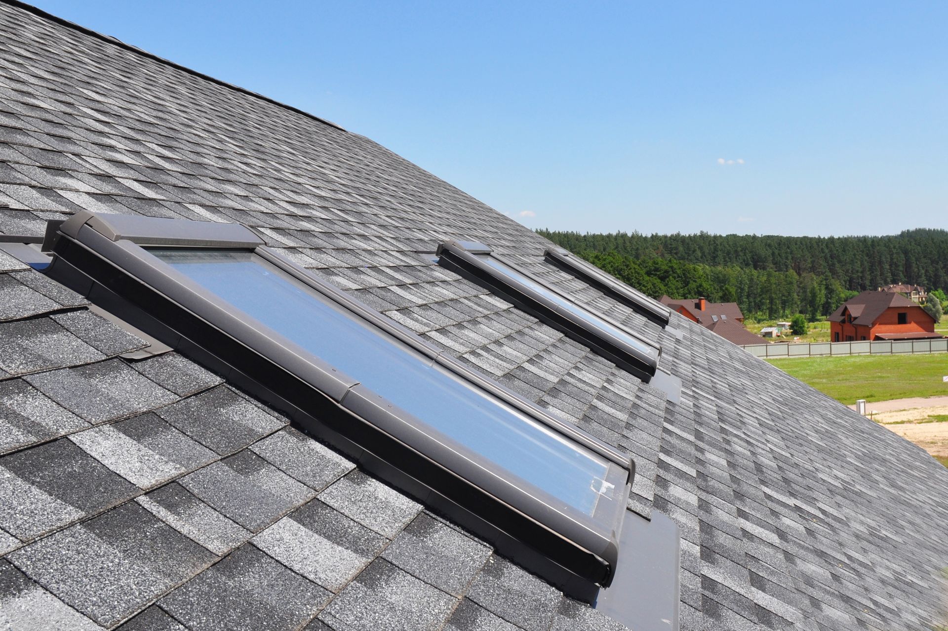 Rooftop skylight on a gray shingled roof under a clear blue sky