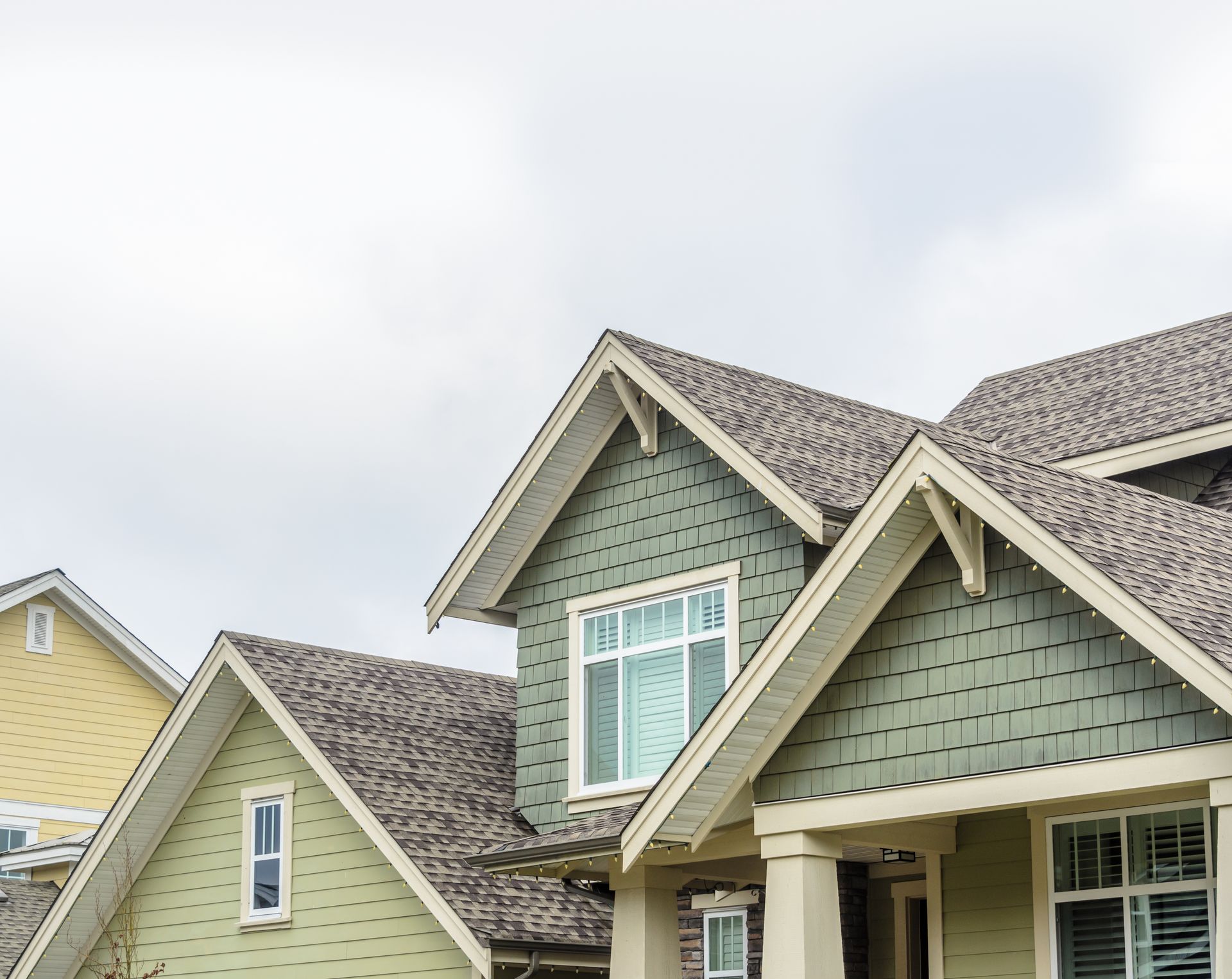 Row of suburban houses with gray shingled roofs and pale green siding under a cloudy sky