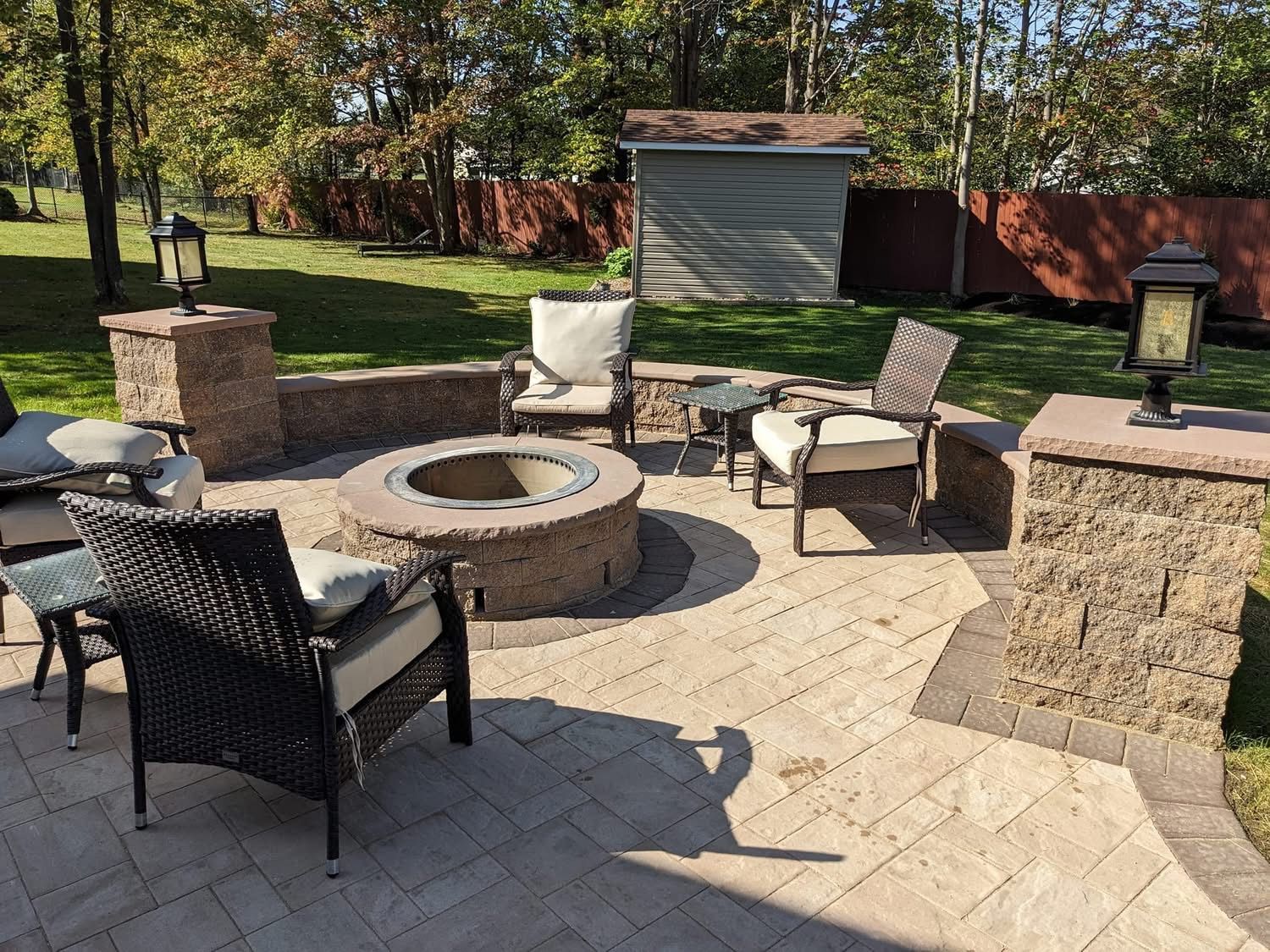 Patio with fire pit, seating, and decorative pillars in a backyard setting.
