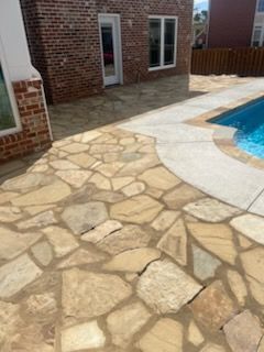 Stone patio next to a pool and brick building. Light-colored stone is used for the walkway.