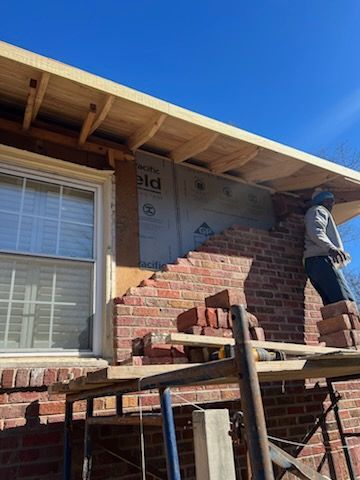 Bricklayer working on a building's brick facade repair near a window, with scaffolding set up.