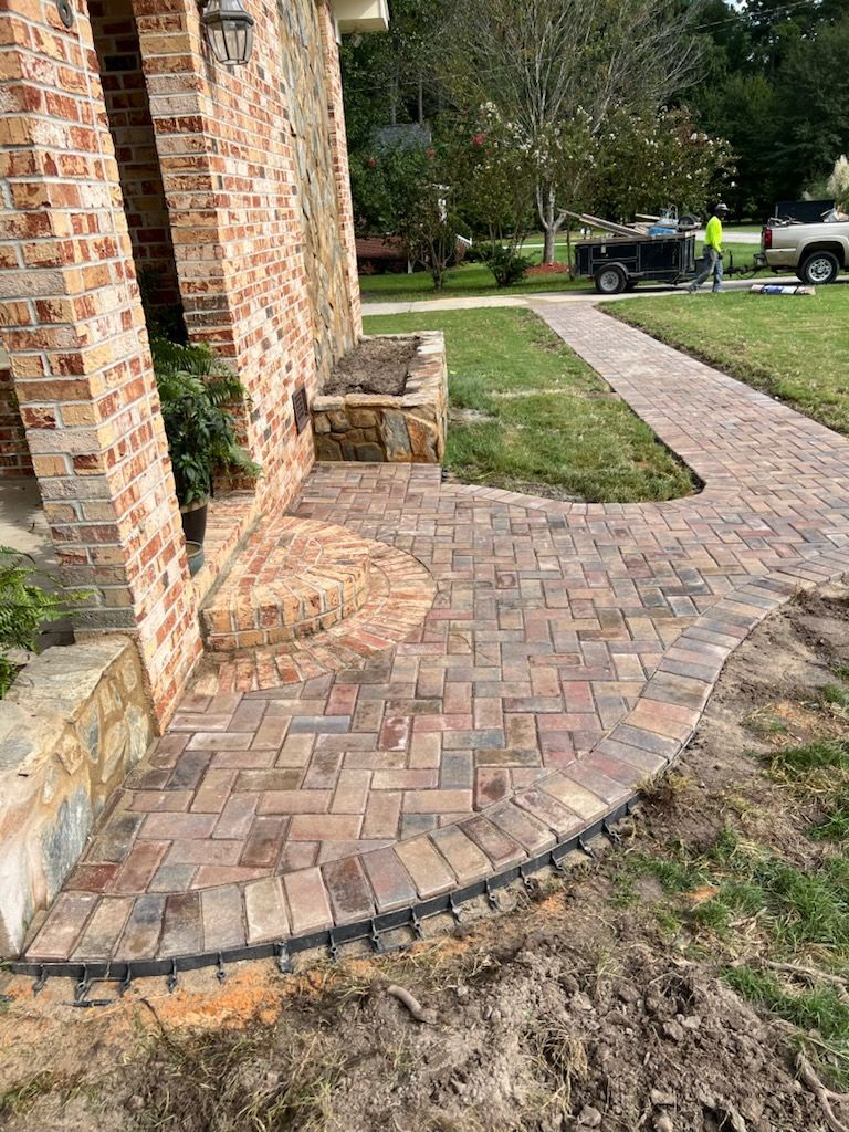 Brick walkway leading from a house entrance to the lawn. Pathway is curved and has black edging.