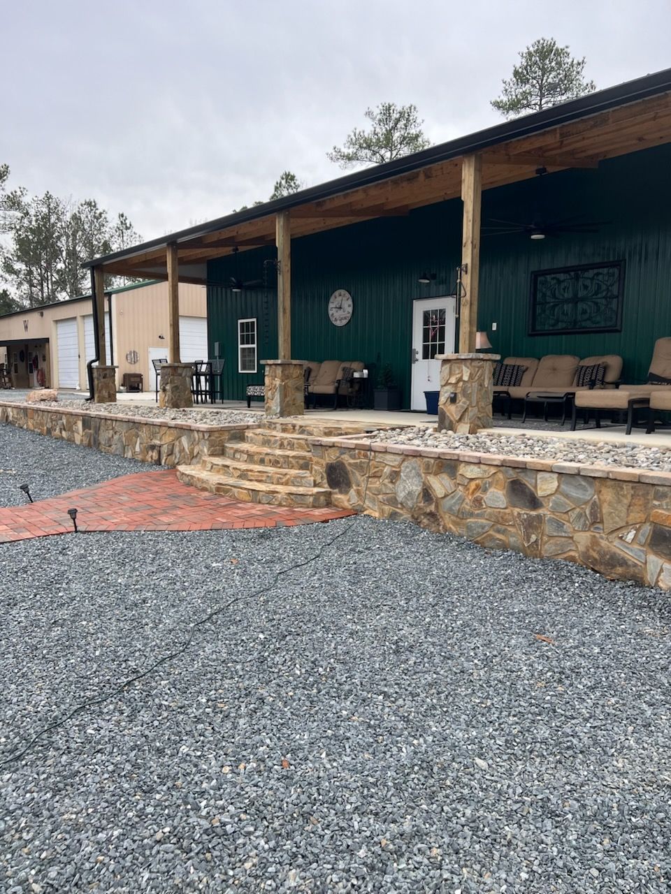 Green building with porch, stone facade, gravel parking area, and brick pathway.