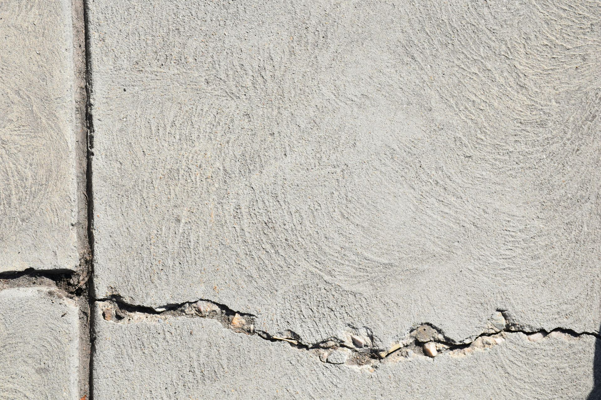 Gray concrete sidewalk with a large crack running through one of the sections.