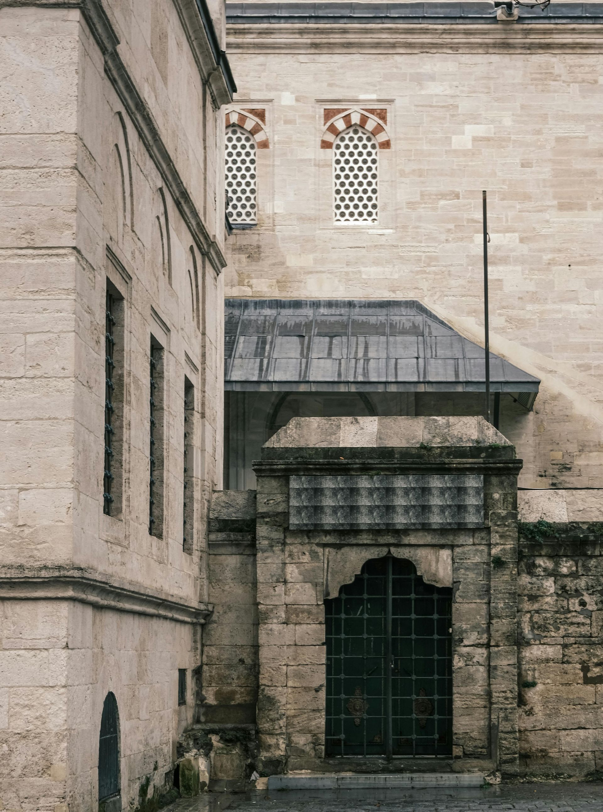 Stone buildings, arched gate, barred window, two upper windows with patterned designs, outdoor.