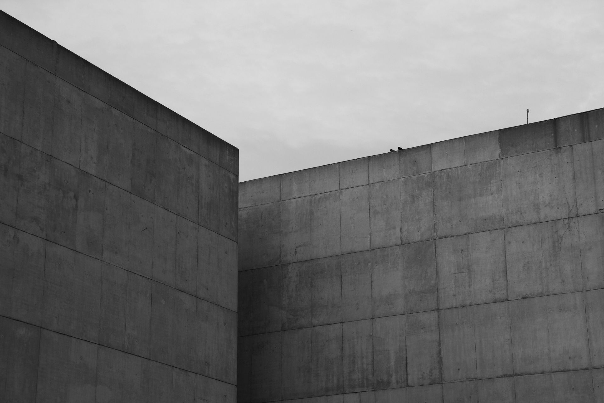 Two gray concrete walls meeting at a right angle under a cloudy sky.