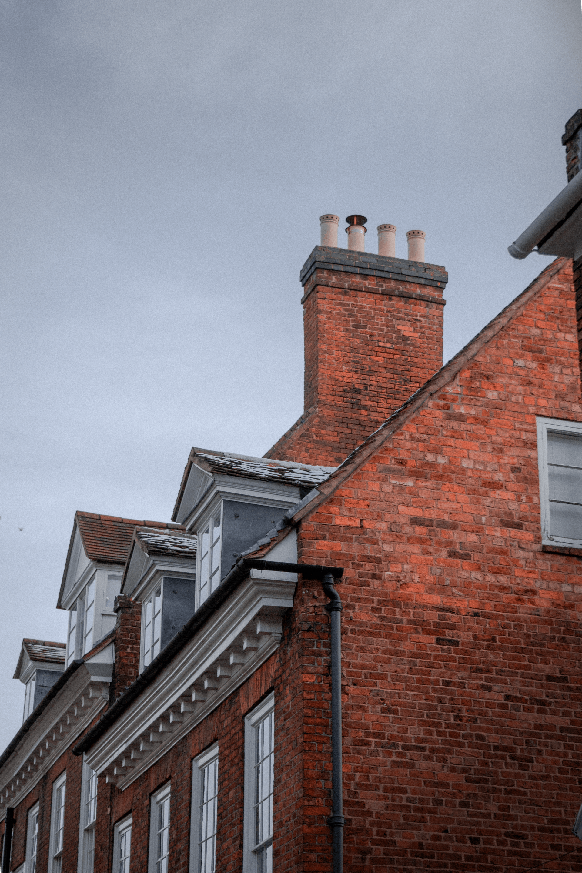 Red brick buildings with dormers and chimney stacks against a cloudy sky.