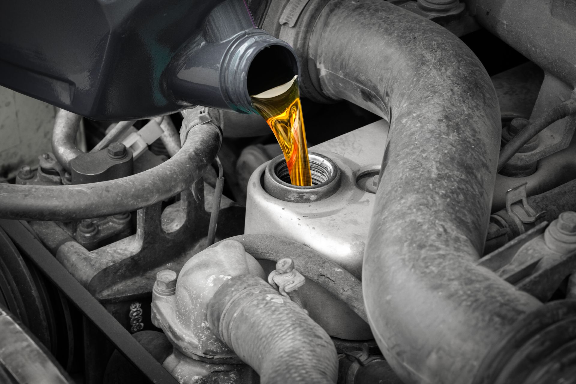Oil pouring into a car engine from a bottle, with a monochrome engine bay and amber fluid.