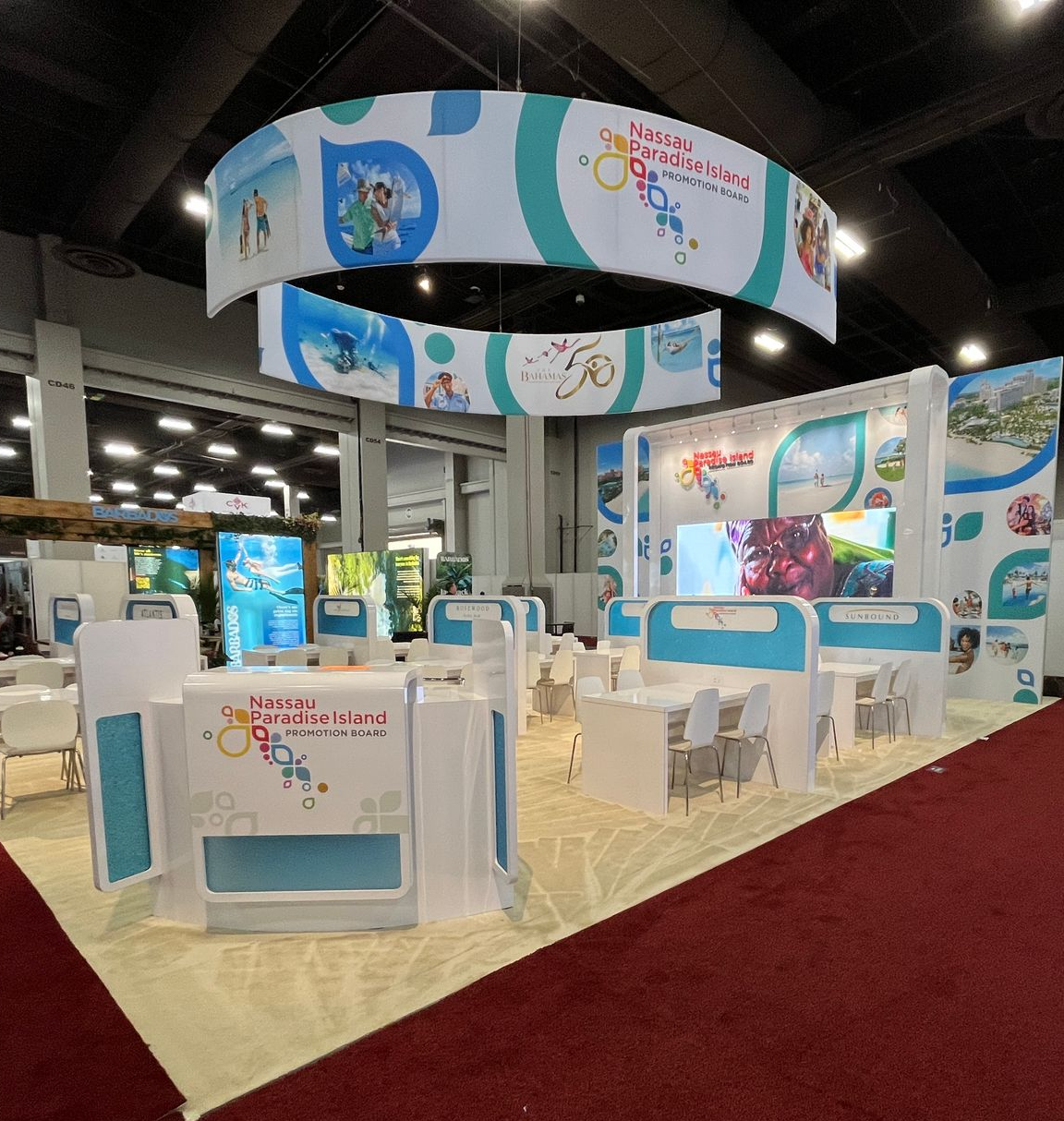 Bright blue-and-white trade show booth with hanging banners, display counters, and chairs on an expo floor