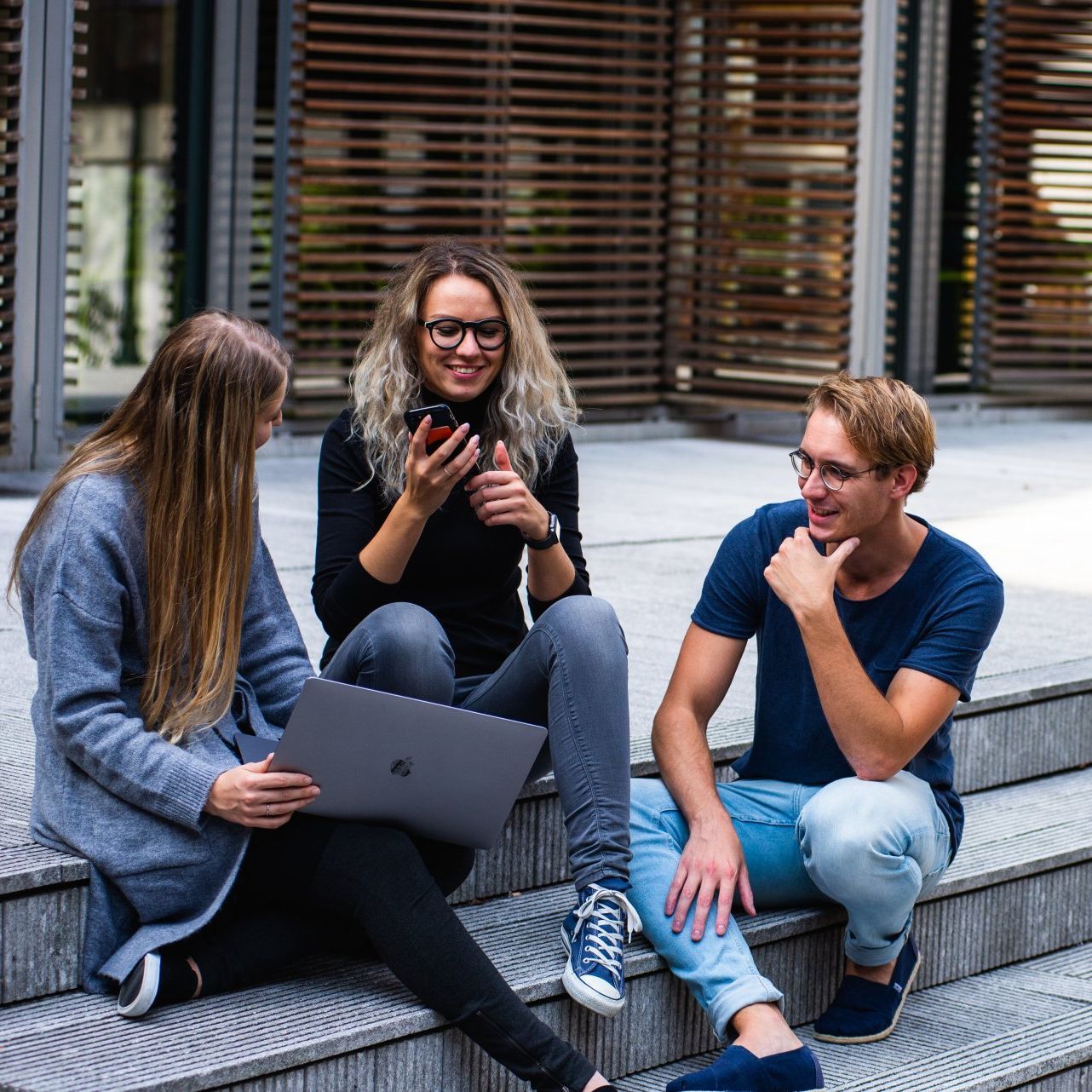 Drie mensen zitten op de trap met een laptop en een mobiele telefoon.