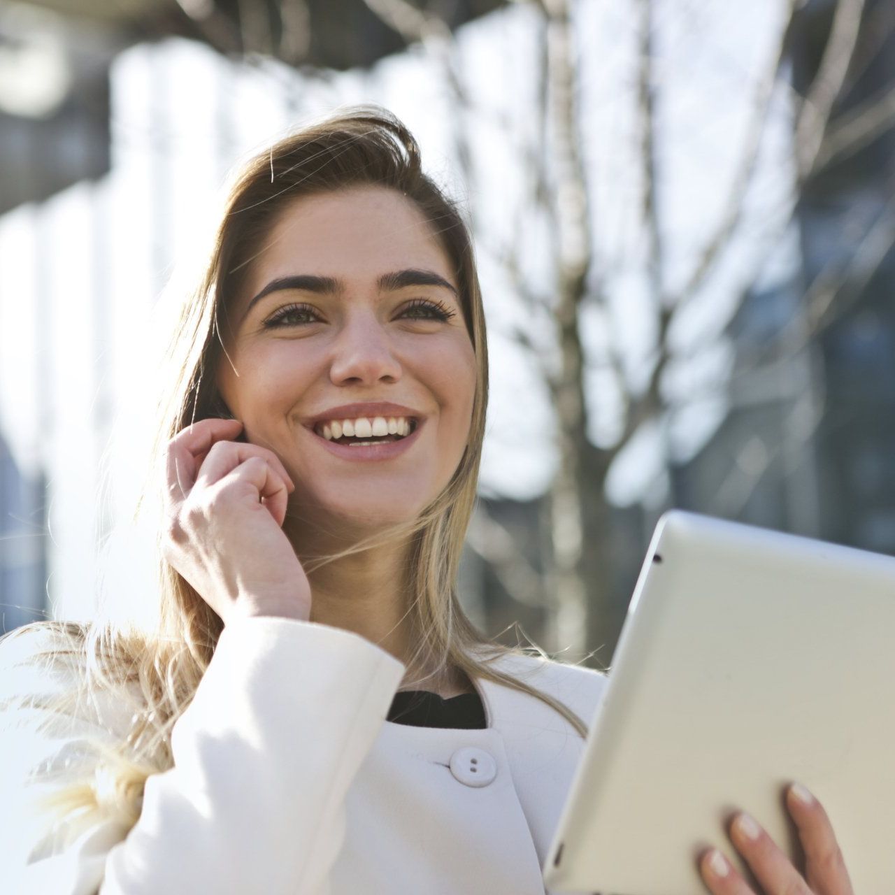Een vrouw lacht terwijl ze een tablet vasthoudt en op een mobiele telefoon praat