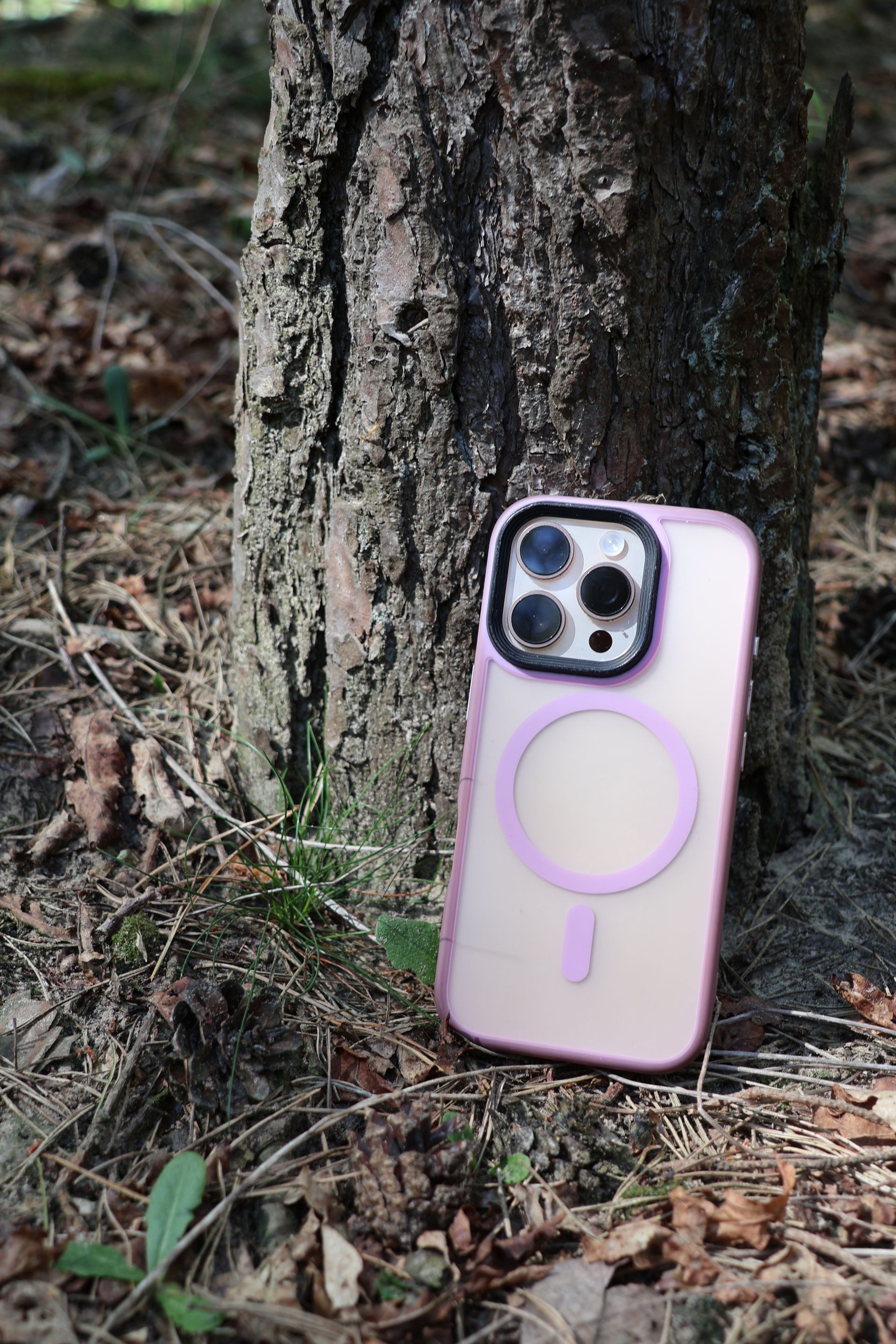 Roze iPhone-hoesje leunend tegen een boomstam in een bosrijke omgeving.